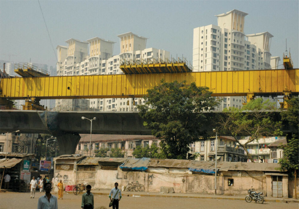 Daylight image of an urban skyline in the background with a yellow, elevated highway under construction in the foreground with people walking below. 