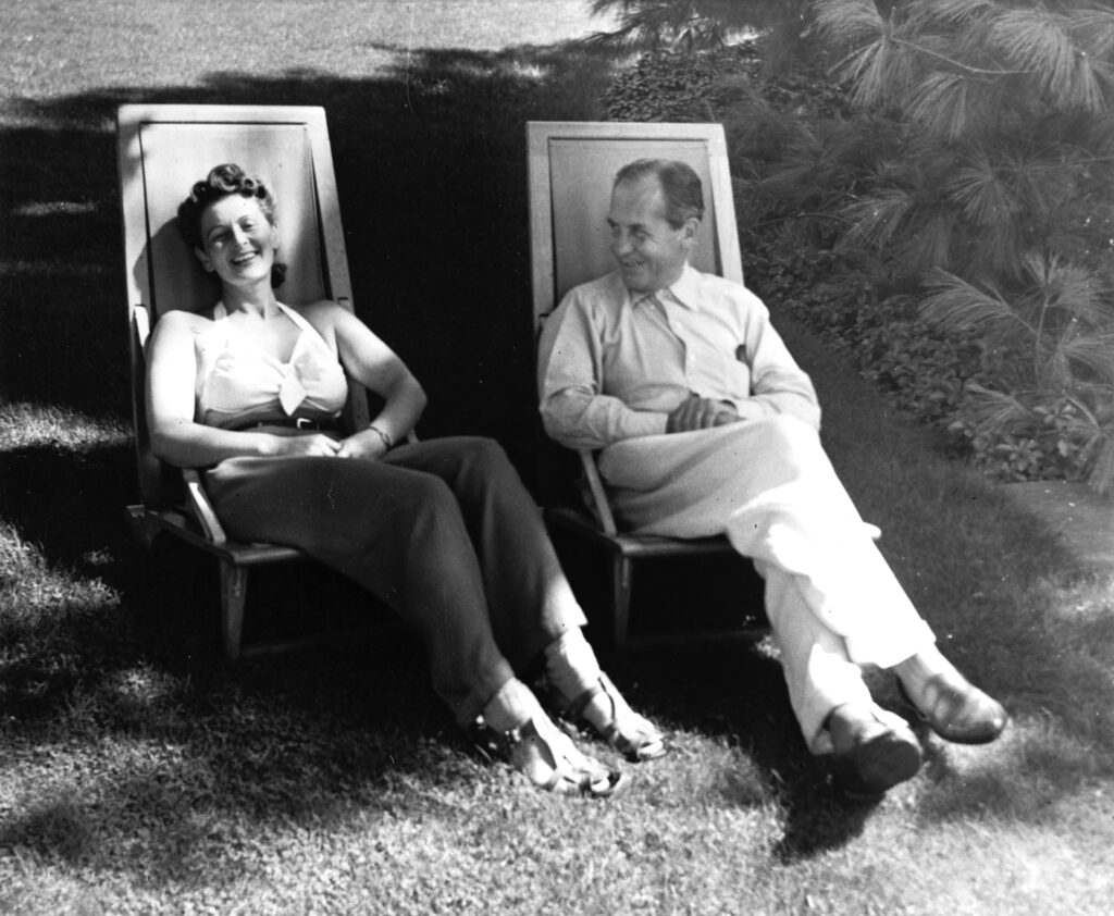 Black and white photograph of a man and a woman outside in the sun sitting in lounge chairs