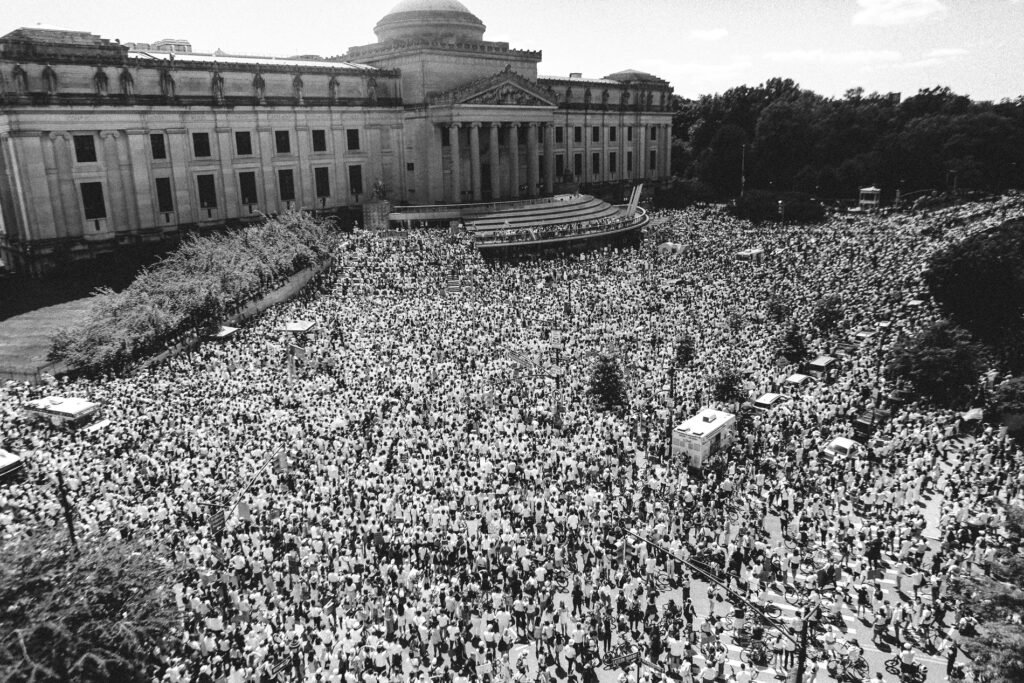 Black and white photograph of crowds of people in front of a wide government building with pillars and a dome