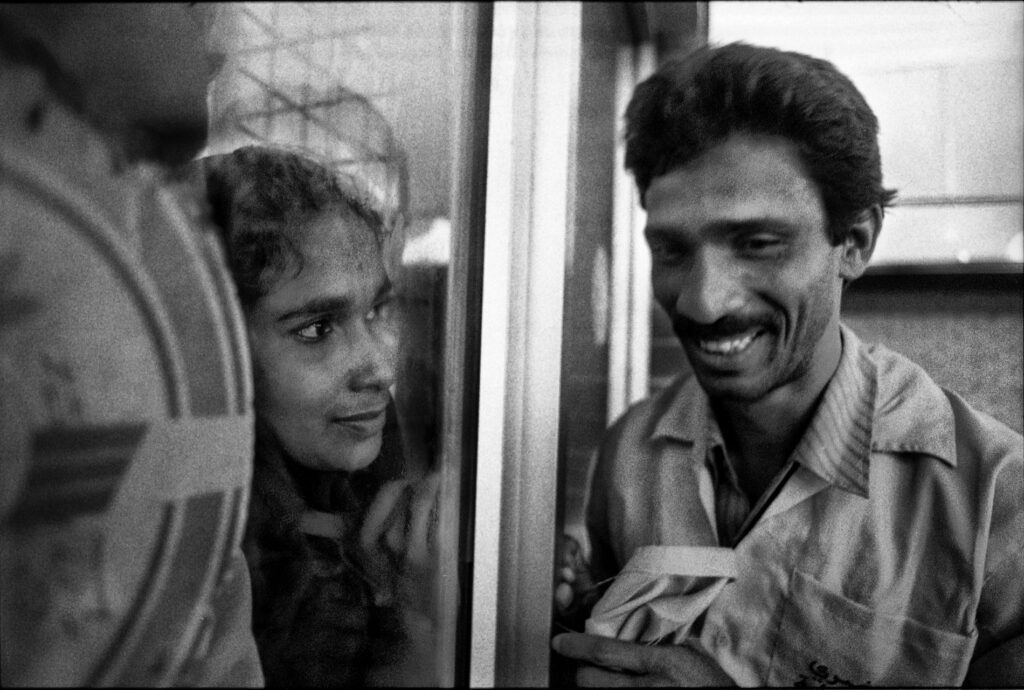 Black and white photograph of a woman looking through a man who is smiling through a glass door