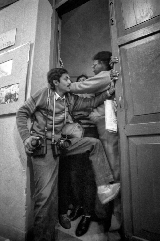 Black and white photograph of three men in a doorway. One of the men has cameras around his neck and is being prevented from entering.