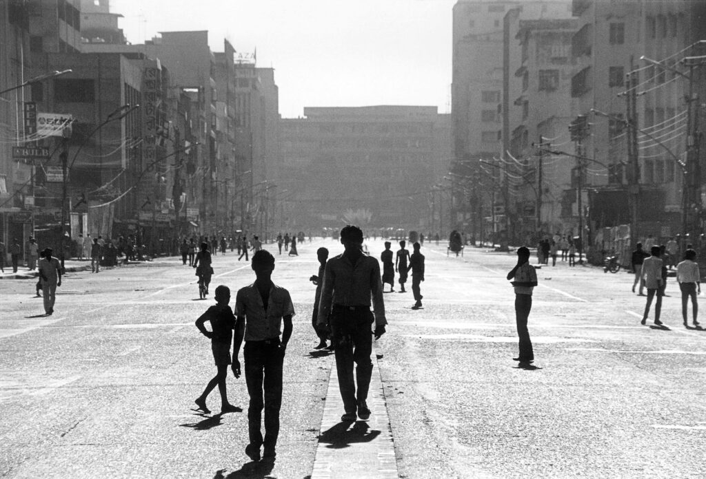 Black and white photograph of an urban setting with buildings on either side of a road with people walking