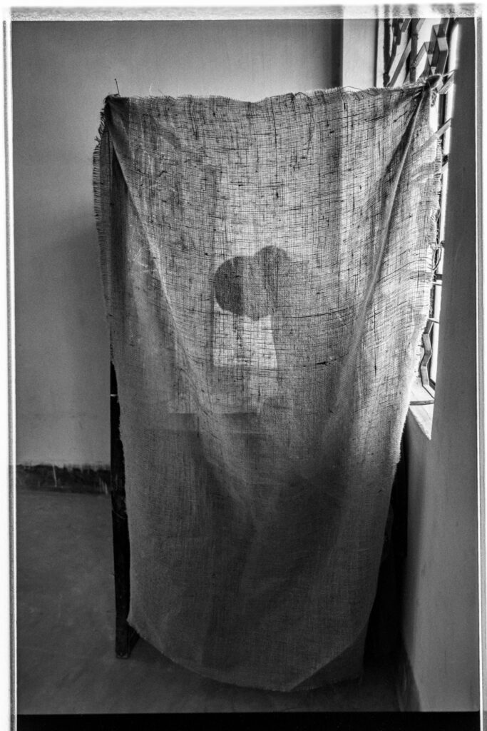 Black and white photograph of a person's silhouette behind a linen cloth curtain