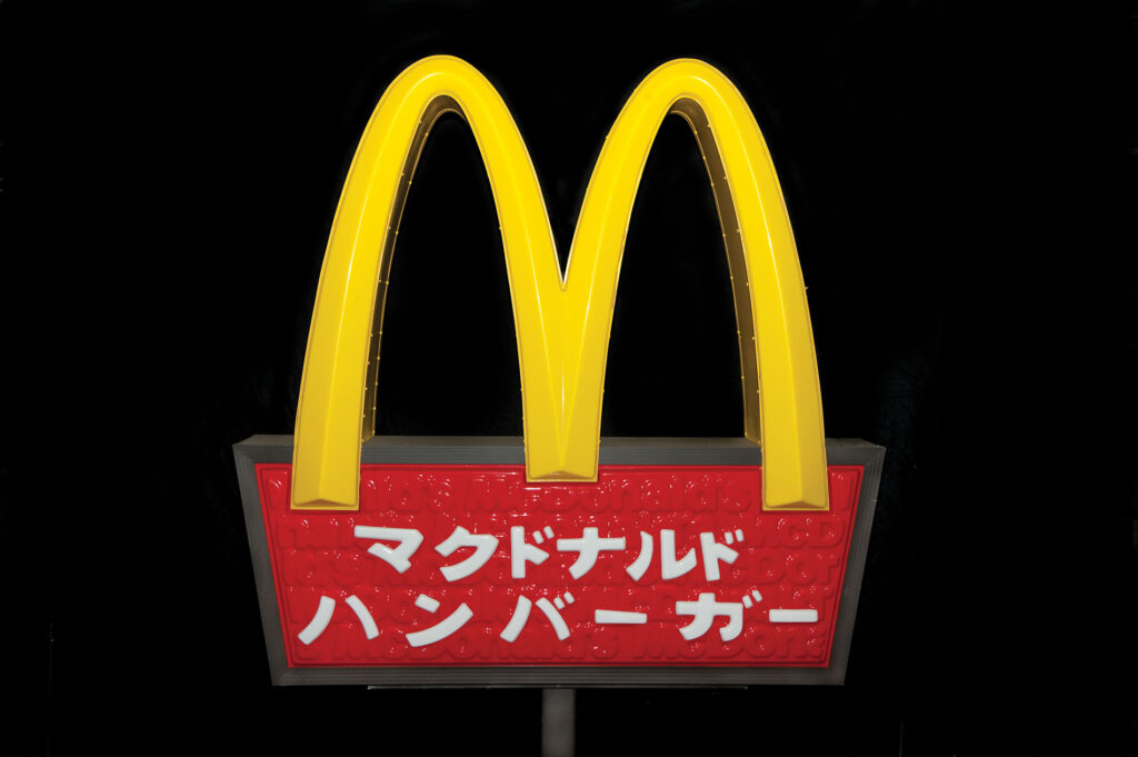 Yellow "M" for the restaurant chain MCDonalds over a red bowl with white writing in Japanese on a black background. 