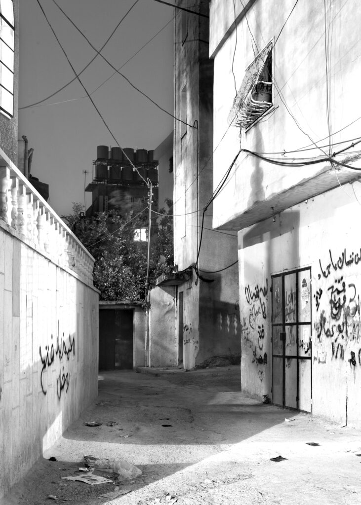 Black and white night scene of an alley between two buildings with black graffiti on the walls