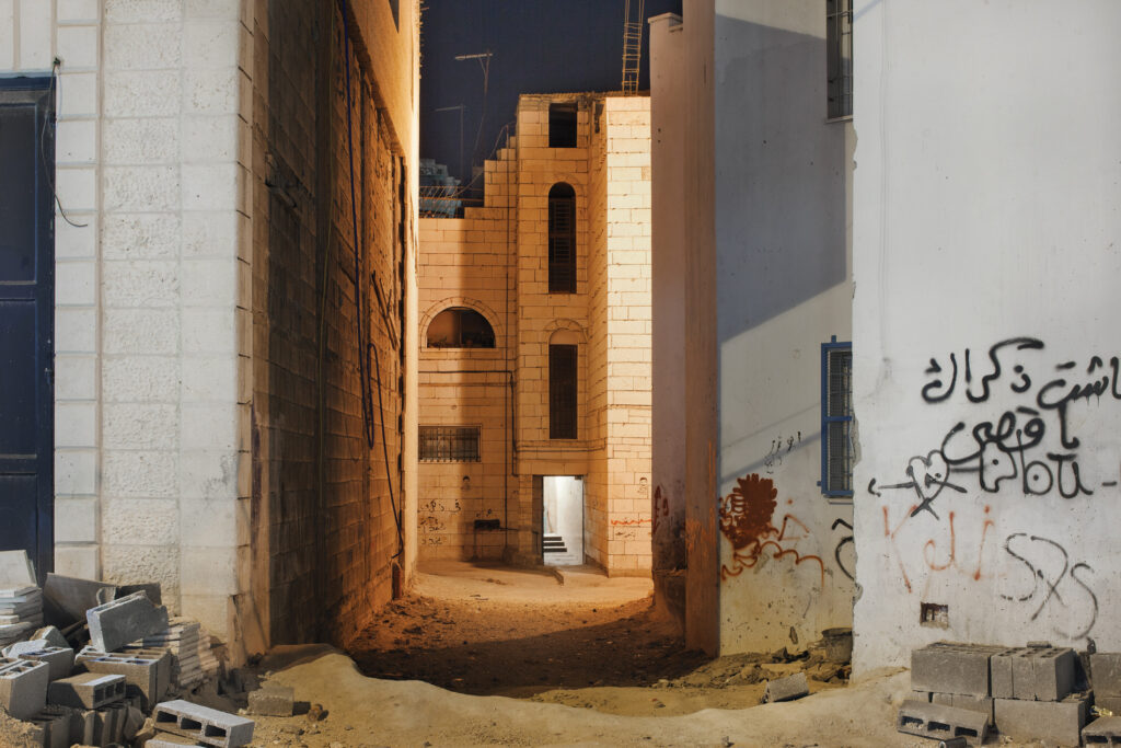 Night view down an alley between buildings with graffitti on walls and sand on the streets
