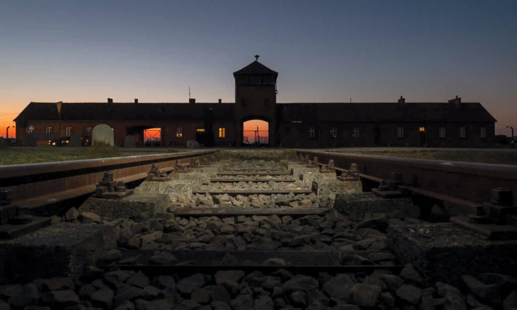 night view of a barn with the sun setting on the other side in front of train tracks