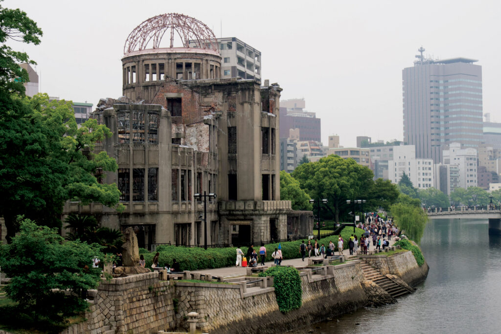 shelled out building along a river with people walking on the sidewalk between building and water