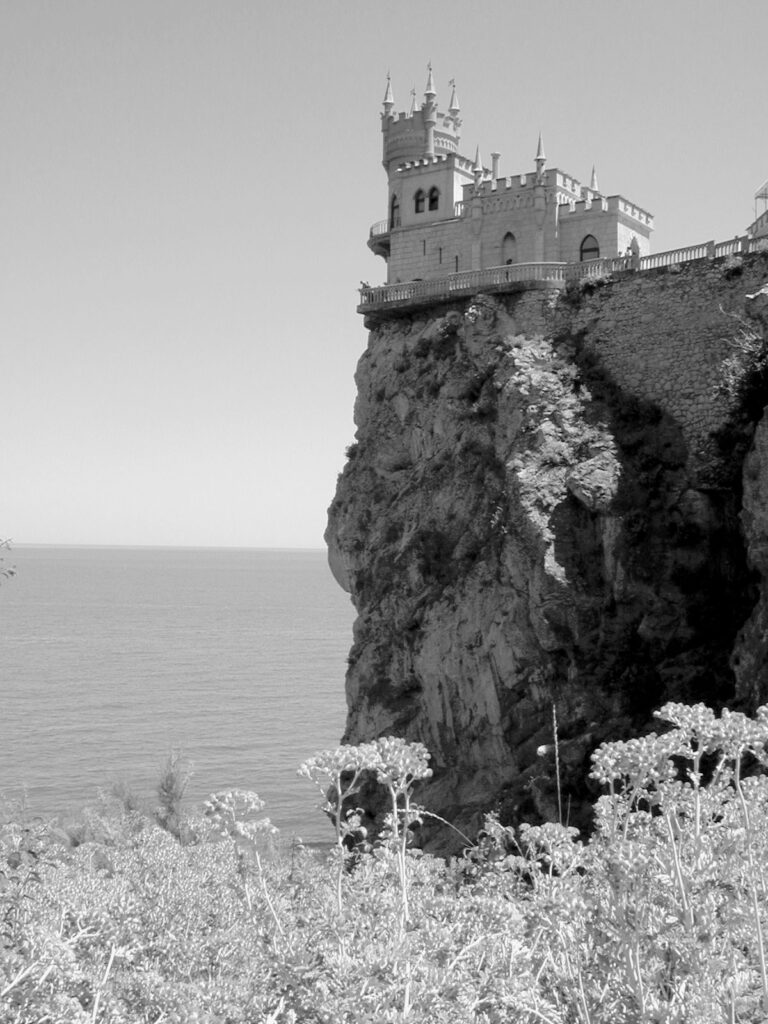Stone structure on the edge of a tall cliff with water below and wildflowers in the foreground
