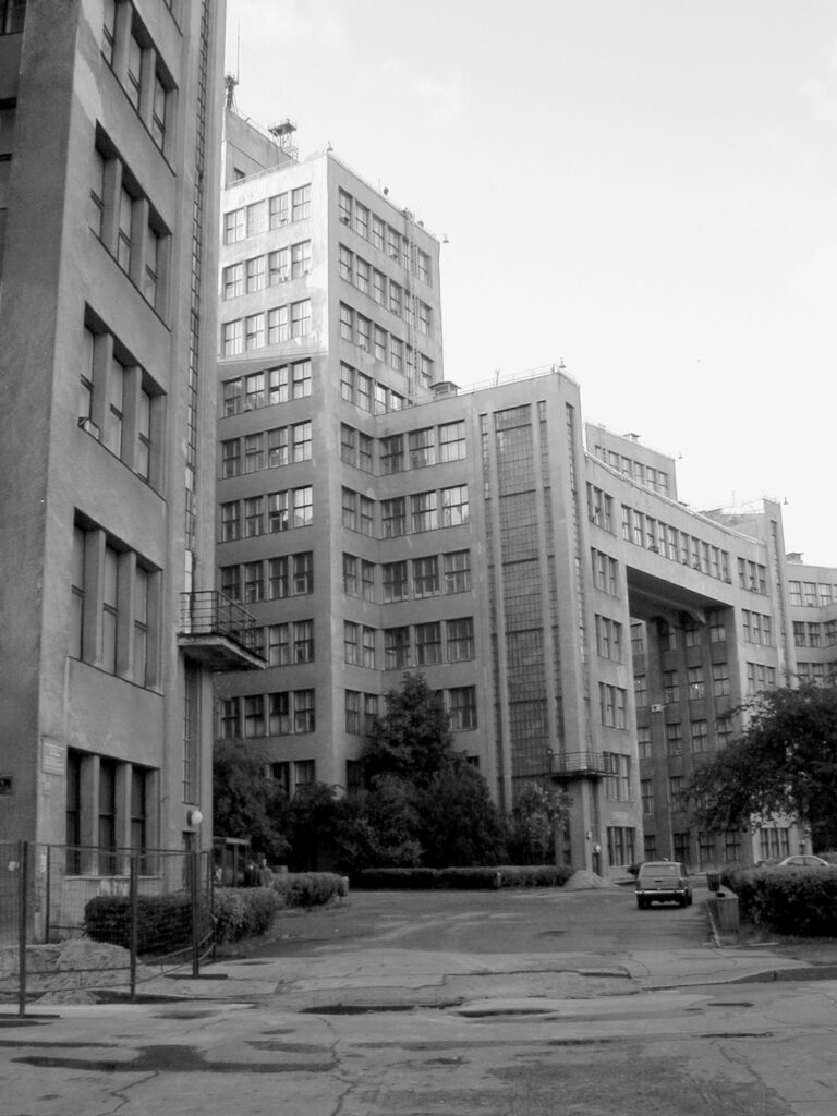 Urban setting with tall buildings, a beat up road, and a car