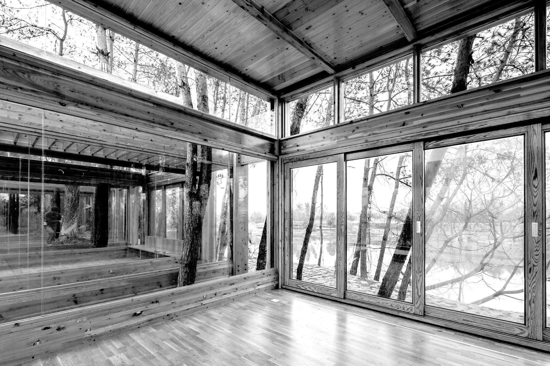 Black and white photograph of the interior or a room with walls made of windows that provide a view of trees
