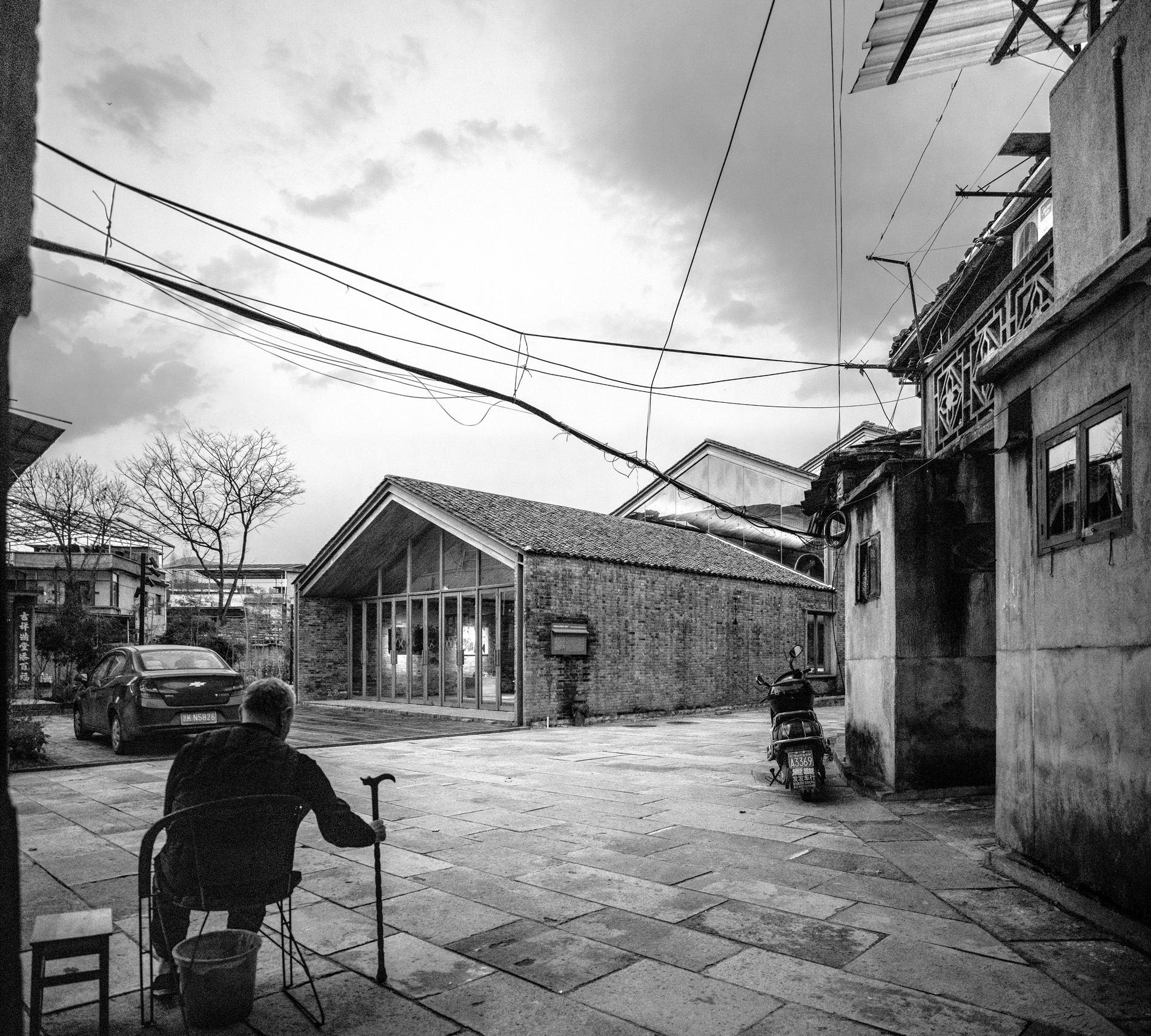 black and white photograph of an elderly man walking through a courtyard toward a building