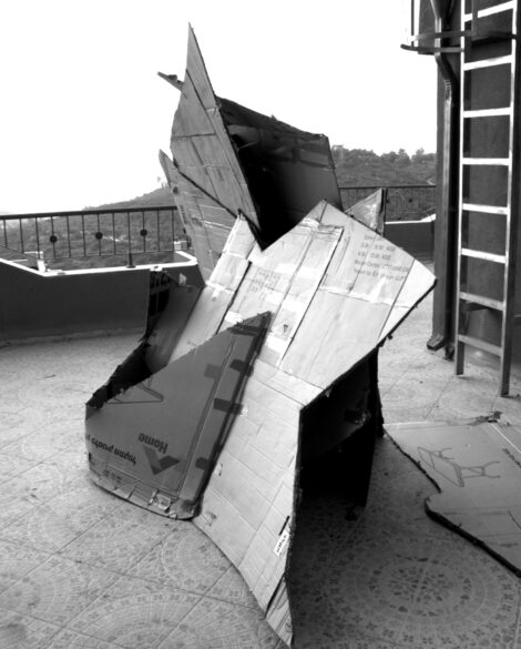 black and white photograph of a sculpture made of cardboard on a balcony with a ladder to the right