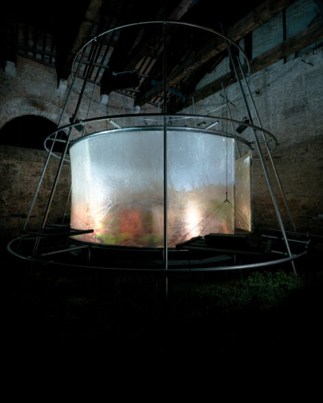 Photograph of a circular metal and glass structure against a brick background with plants inside