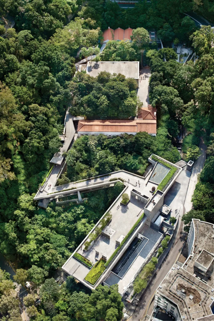 Arial view of a building with red roofs and walkway that zig zags through a lush forest.