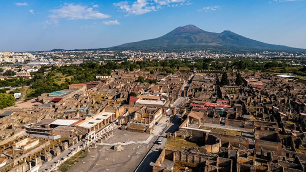 Aerial drone image of excavated ruins of Pompeii with Mt Vesuvius in background.