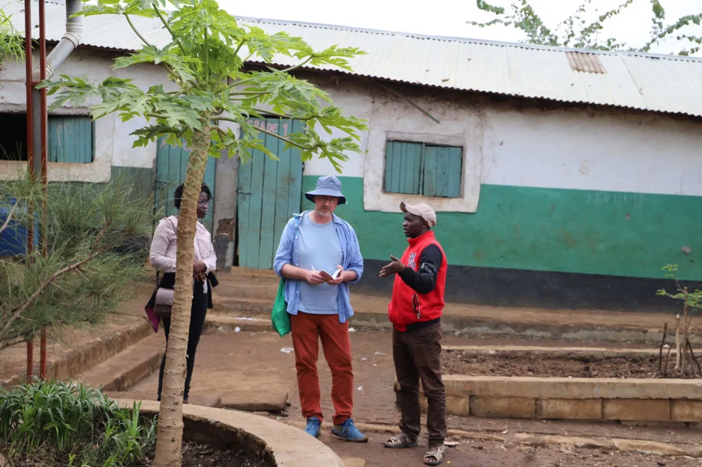 Three people stand in front of a building painted teal green and white.