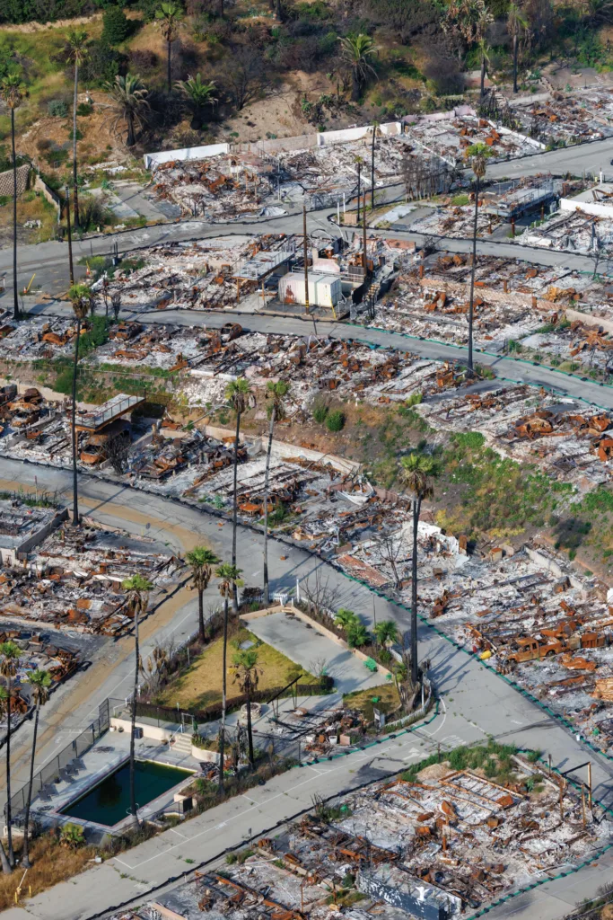 Aerial view of a streets in a neighborhood showing charred remains of homes and palm trees.