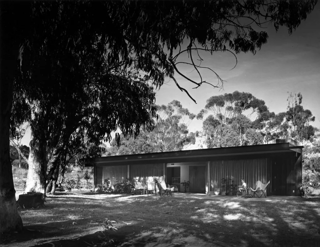 Black and white photograph of a single story home surrounded by trees.