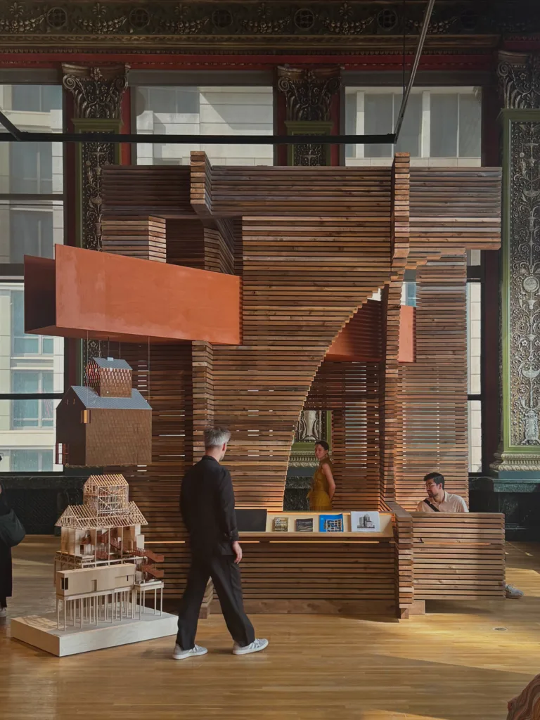 Wooden architecture installation with people walking around it.