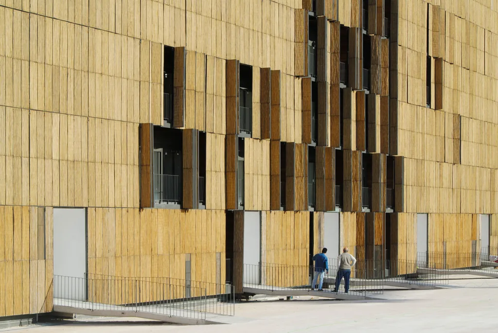 Two people stand outside a large apartment building with many shutters on the exterior. 