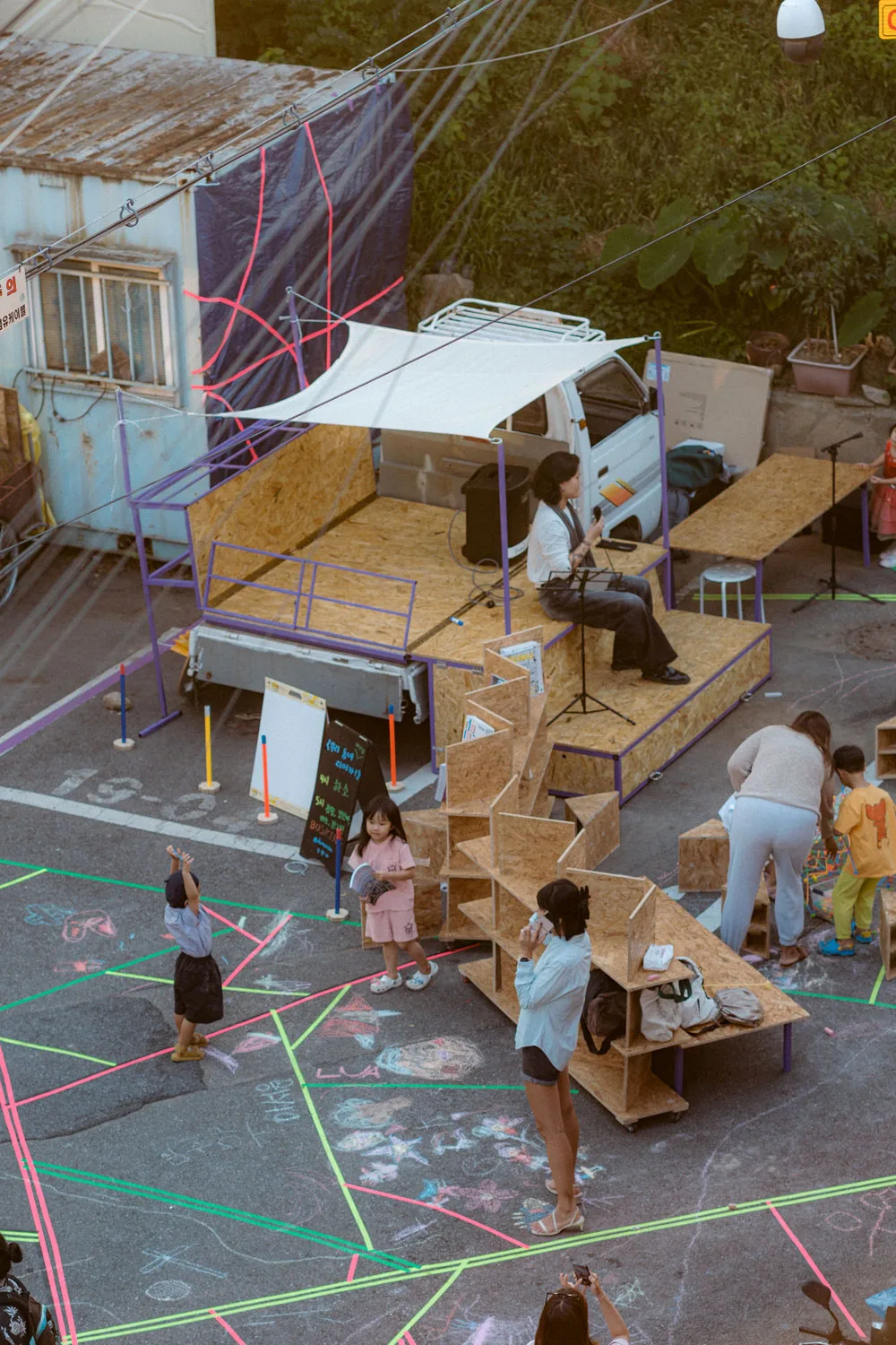 A group of people gather around a wooden platform that has folded out of a minitruck. 