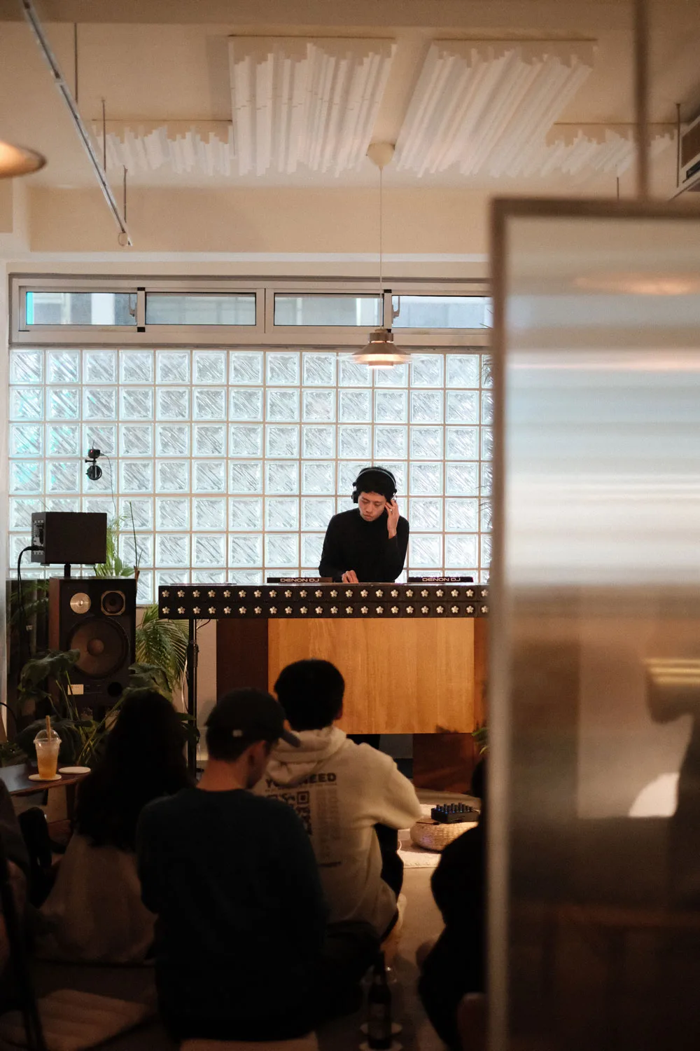 A DJ stands behind a counter in a room with a few people sitting on the ground. 