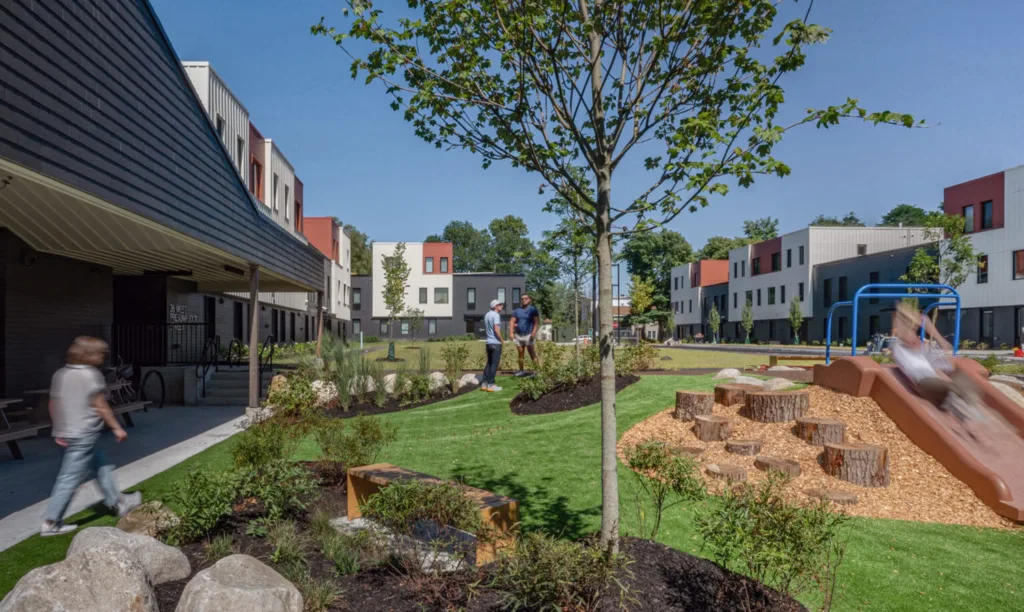 Courtyard of a housing development with a playground, grass, and trees.