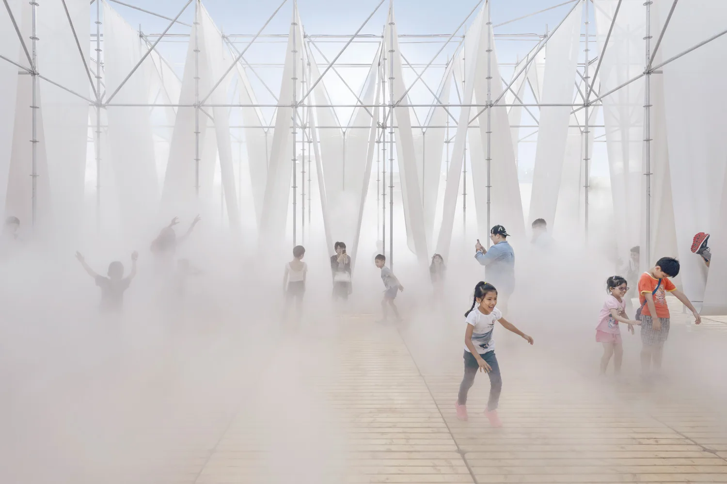 Children Play in a structure of metal poles and white fabric filled with a cloud of mist. 
