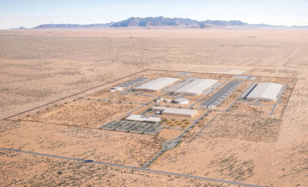 An aerial view of a data center complex of large, low gray buildings in a desert landscape.