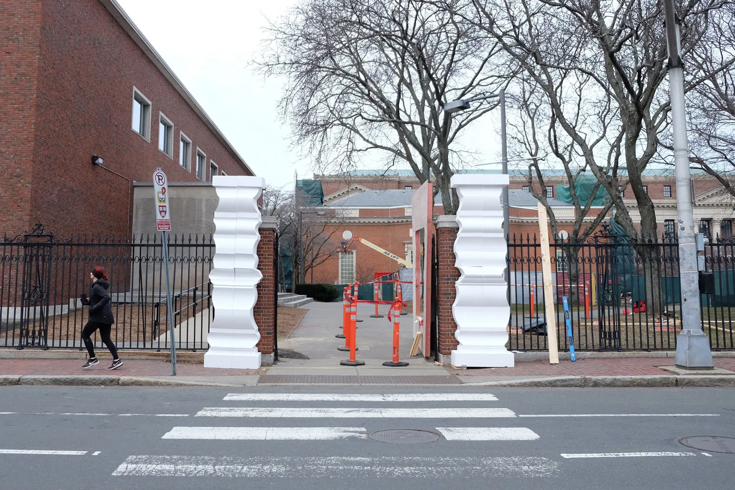 photograph of the construction of columns and a gate with orange cones in front of a road with a cross walk