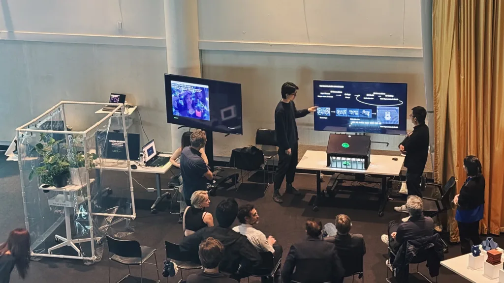 People watching student present and pointing to a large computer screen.