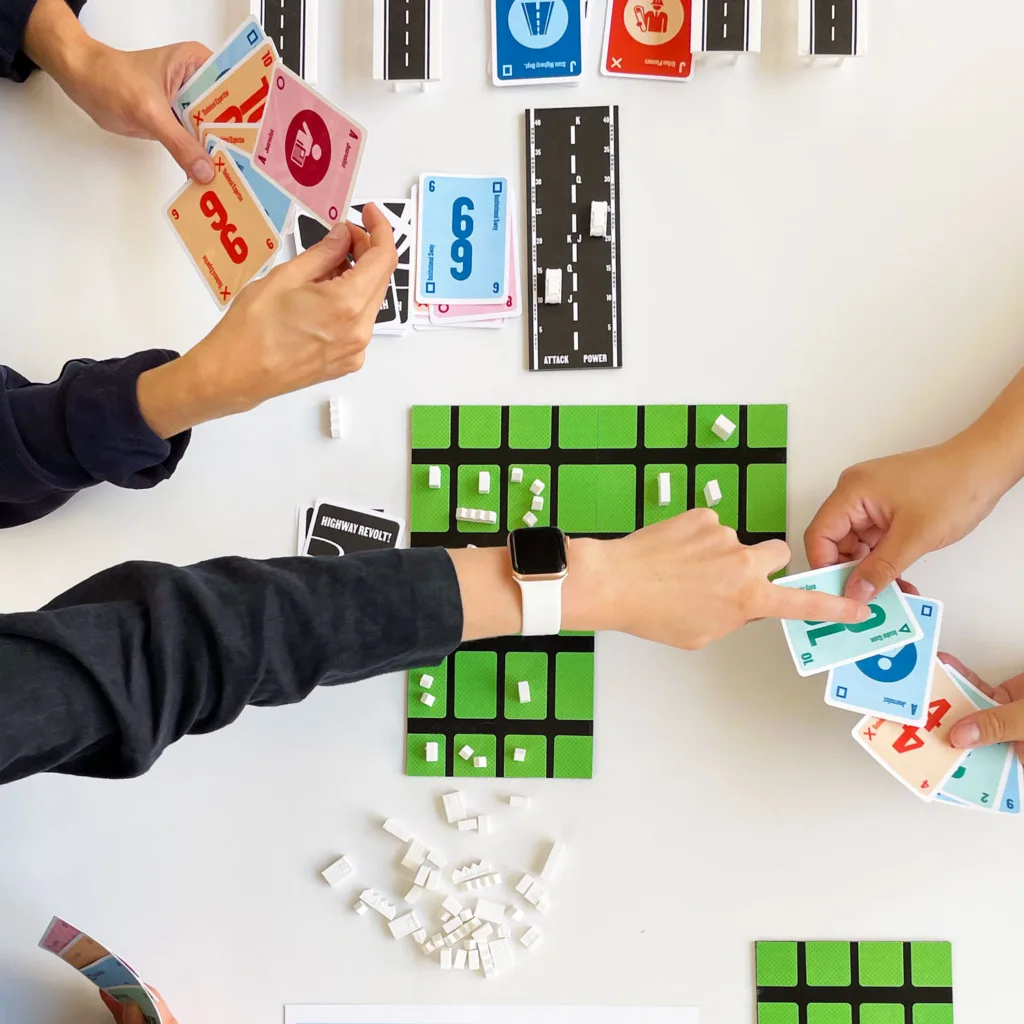 Three sets of hands play a card game with a green board.