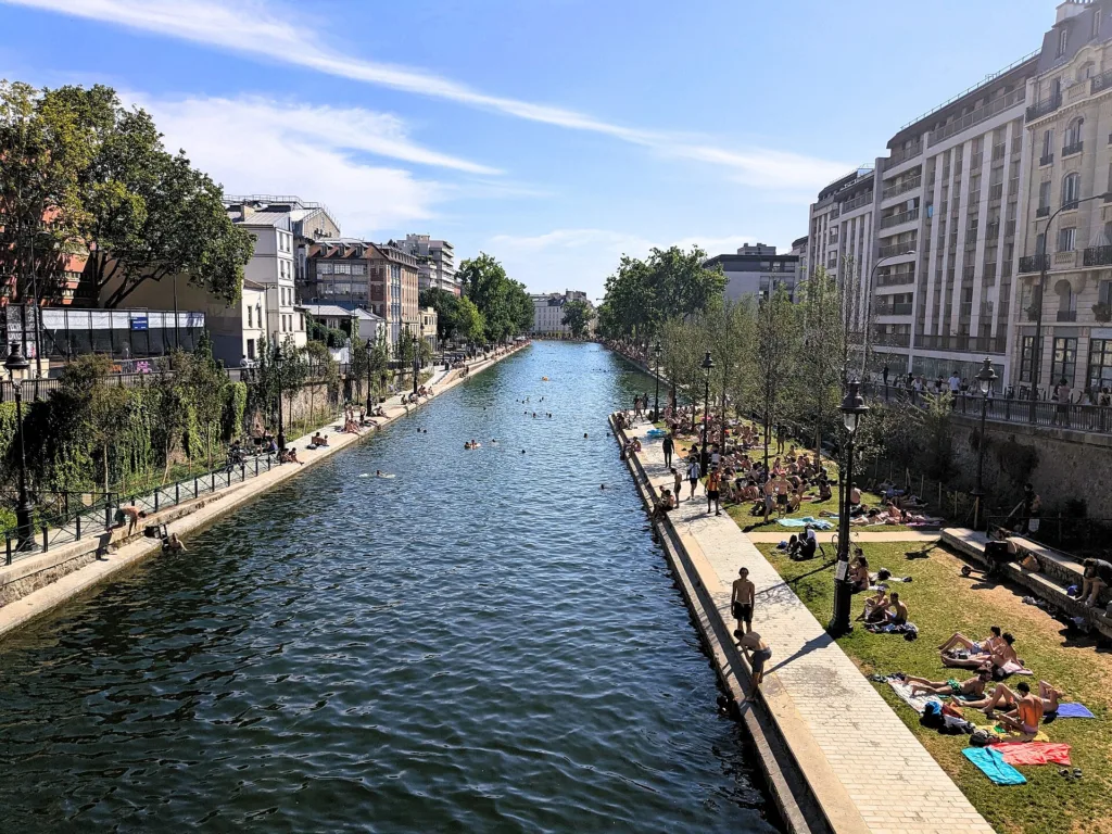 People swim in the water, and sunbathe and walk on the banks of Paris's Canal Saint-Martin.