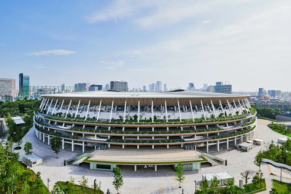 Aerial view of a large landscaped oval stadium with a city skyline in the background.