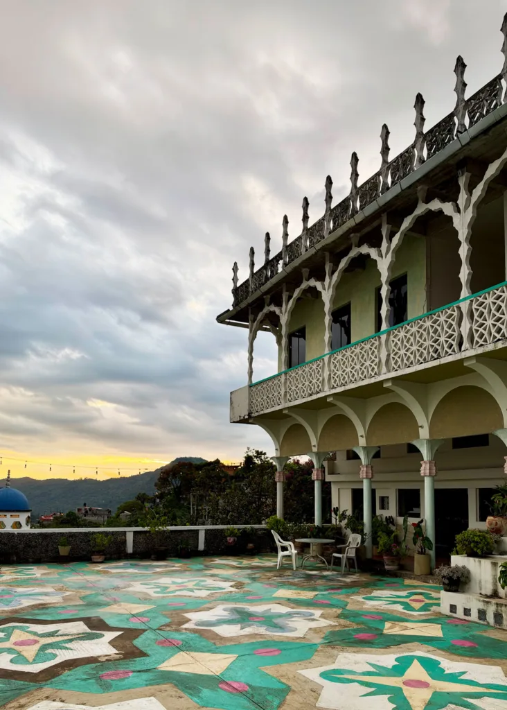 A concrete building with balcony, colorful patio, and view toward the mountains.