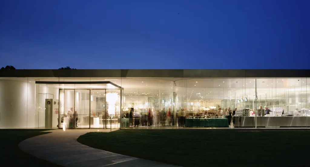 Transparent glass pavilion with people inside at night.
